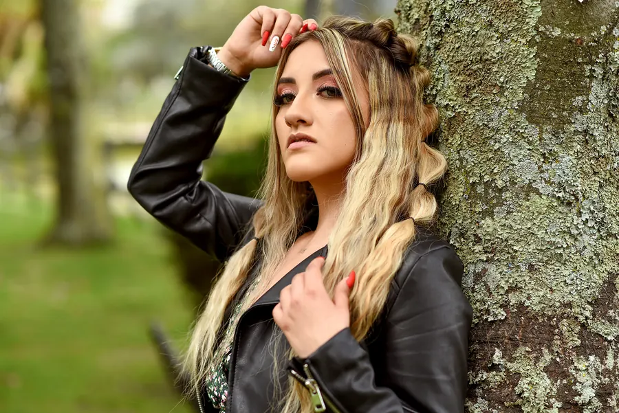 Modelo de Red Paradise VIP en una sesión de fotos al aire libre, apoyada en un árbol en un parque